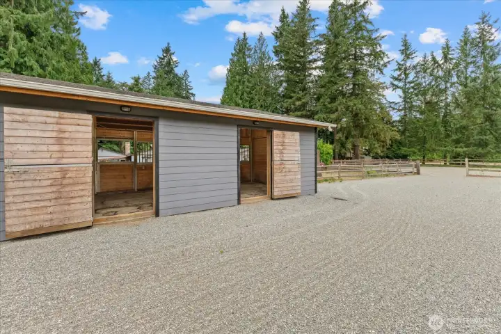 Back side of the stall barn with Dutch doors, riding paddock with mud-free hoof-grid footing under the sand and gravel.