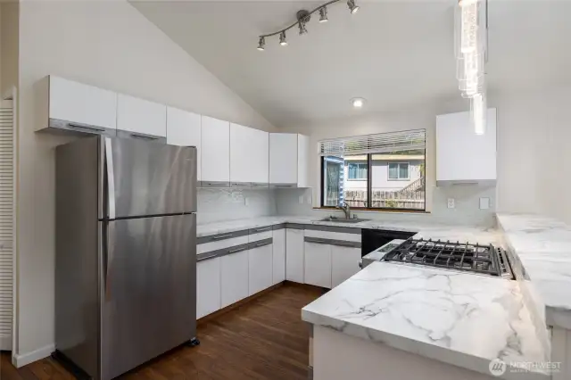 A gas oven/range, window overlooking the fully-fenced back yard, a pantry to the left of the refrigerator.