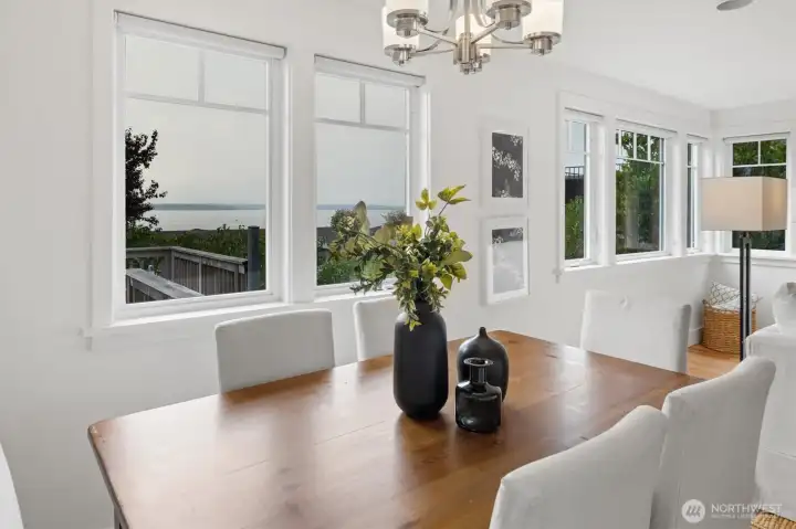 From this vantage, the dining room showcases its scenic outlook with water views framed by oversized windows. Natural light enhances the clean, modern design, while the open connection to the living room makes the space equally suited for relaxed gatherings or elegant dinners.