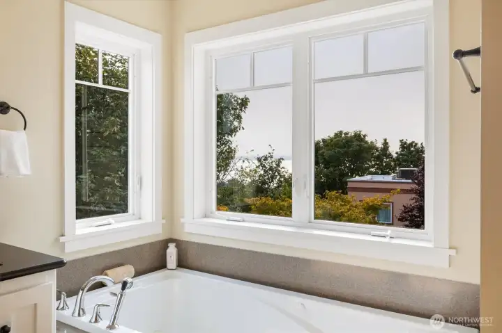 The spa-inspired primary bath features dual vanities, a soaking tub framed by windows, and a walk-in glass shower. Thoughtful finishes and natural light create a serene retreat for daily routines or unwinding at the end of the day.
