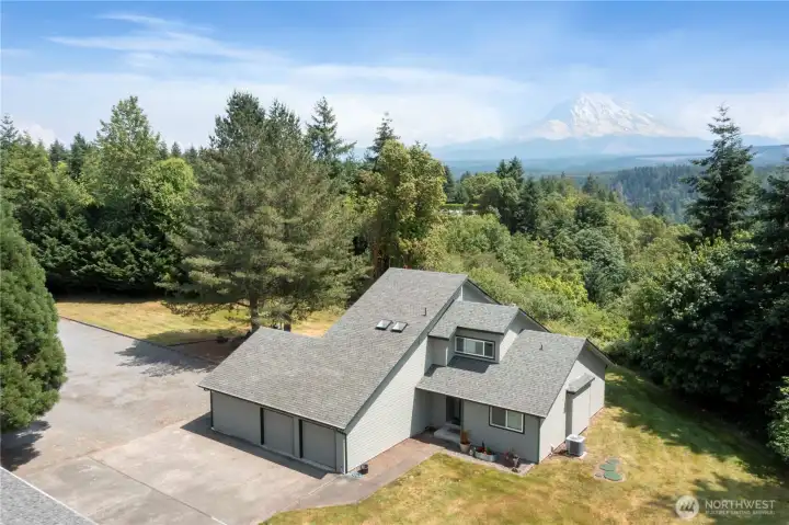 Aerial view of home facing south east with unobstructed view of Mt. Rainier.  Note large paved parking area between home and free standing three car garage.
