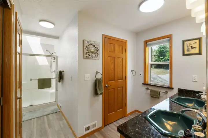 Primary 3/4 bathroom.  Double sink vanity.  Skylights bring in ample ambient light. Door opens into a large walk in closet, and then into a very large walk in attic storage area.