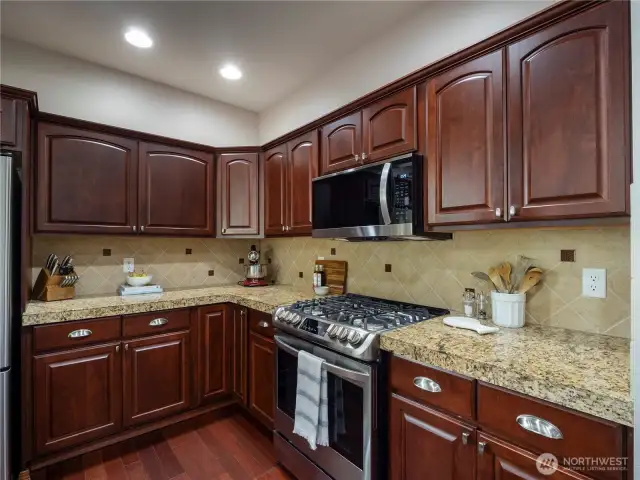 The kitchen features granite tile countertops, tile backsplash, gas range, stainless steel appliances and cabinets with pullout drawers.