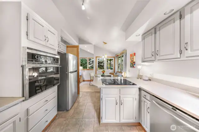 The kitchen island with cooktop faces the adjacent dining space and doors, blending indoor and outdoor living.