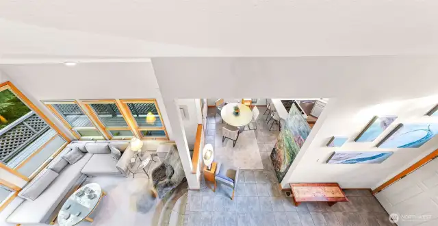 The soaring loft overlooks a light-filled great room, showcasing floor-to-ceiling windows and a seamless flow between dining, kitchen, and living spaces.