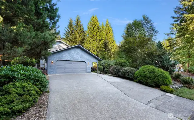 A rare flat driveway leads to a charming shingled façade, nestled among evergreens for privacy and peaceful curb appeal.