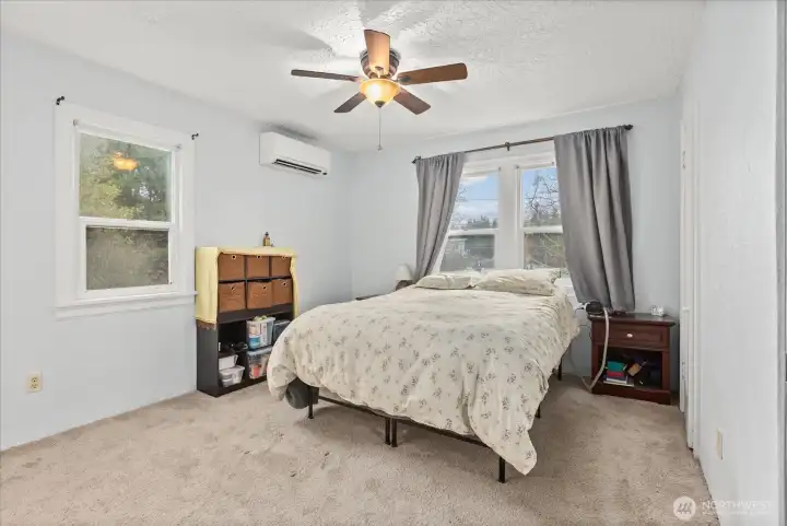 The main-floor primary bedroom is bright and spcious with soft carpeting, large windows and ceiling fan.