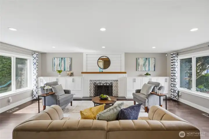 Light-filled living room featuring oversized windows, recessed lighting, custom built-ins, and a cozy fireplace.