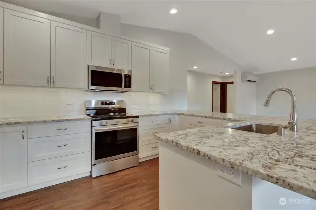 Modern white cabinets with silver appliances and fixtures. clean, sleek and bright. Primary bedroom door is directly behind down a short hall.