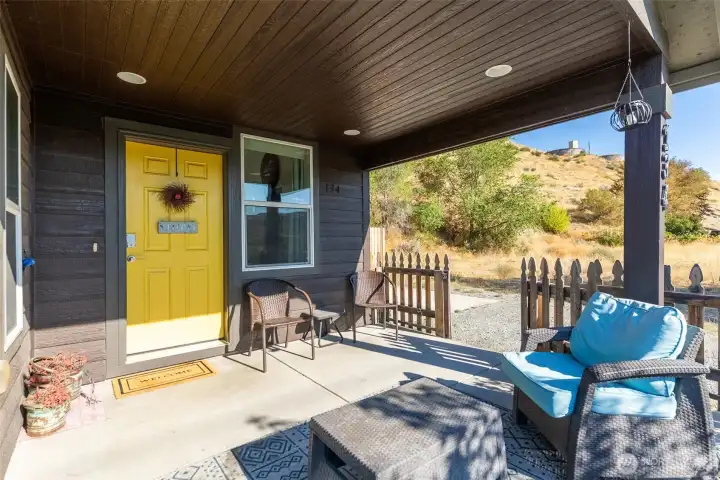 Welcoming covered porch with a sunny yellow door and plenty of space to relax outdoors.