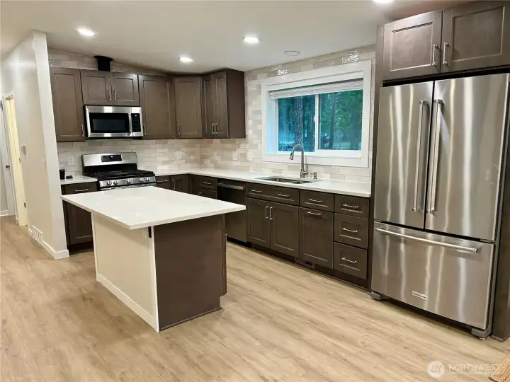 The kitchen boasts new cabinetry, beautiful Corian countertops, and a spacious kitchen island with additional cabinets. Stainless steel appliances complete the modern and functional design, making this kitchen both stylish and practical.