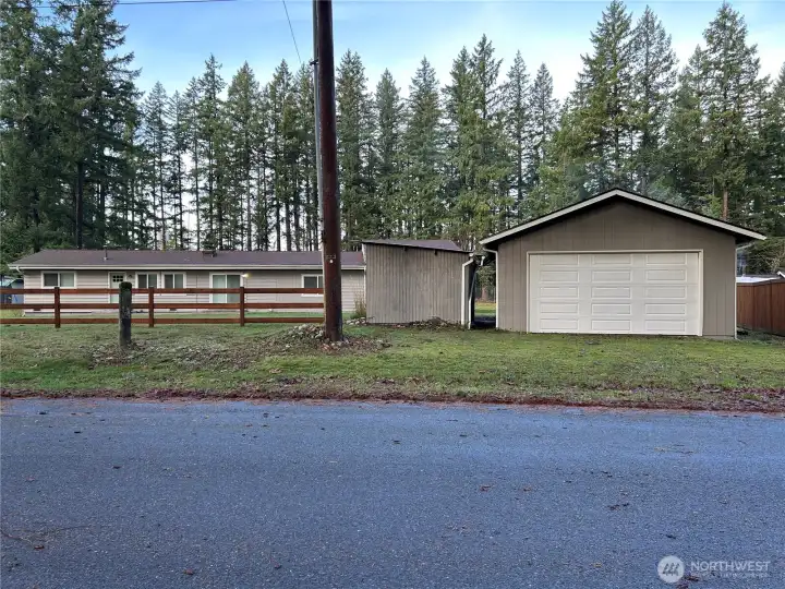 This photo is taken from the street, showing the entrance to the detached garage. Both the garage door and the man door are new. To the left of the garage is a storage shed, and behind that is the pump house for the private well.