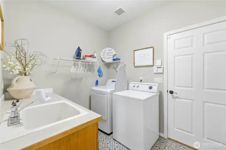 The laundry room has been recently refreshed with new flooring, and the adjacent door leads to a spacious 3-car tandem garage with overhead rack storage.