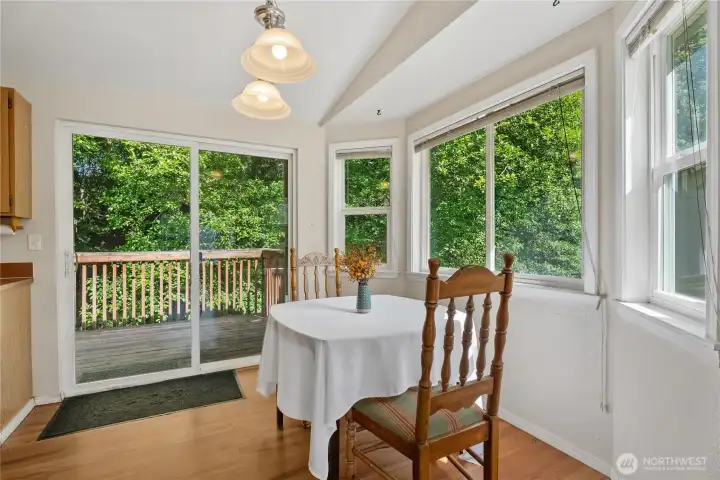 A cozy dining area surrounded by panoramic windows looking out into the peaceful, wooded yard.