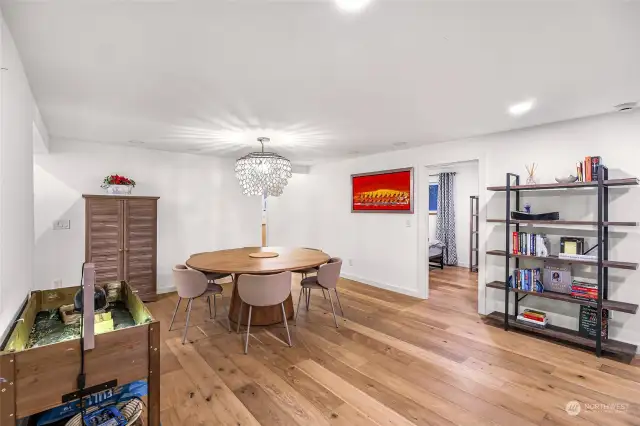 The cozy dining area features a contemporary chandelier, a spacious round dining table, and natural light filtering through nearby windows. A perfect spot for meals or entertaining.