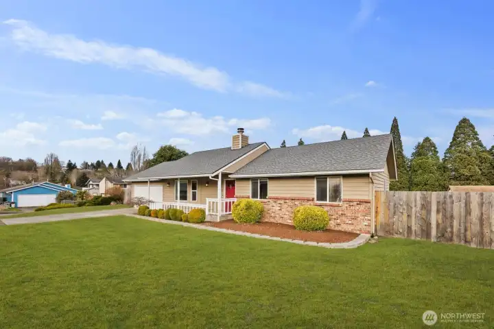 Angled exterior view of single-level home with attached two-car garage, covered front porch, brick and siding façade, and fully fenced yard.