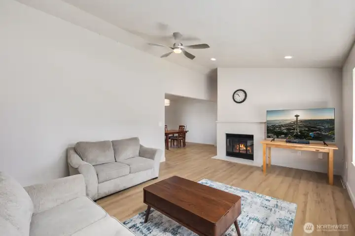 Living room with wood-burning fireplace, ceiling fan, recessed lighting, updated flooring, and open sightline to dining area.