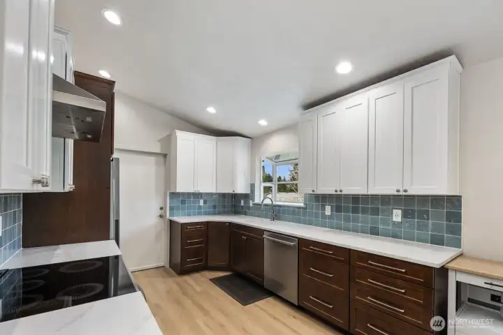Remodeled kitchen with extended quartz countertops, stainless steel dishwasher, under-mount sink with window, recessed lighting, and full tile backsplash.