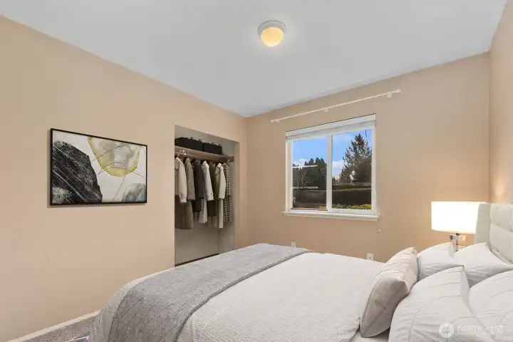 Bedroom with window overlooking backyard, carpet flooring, and open closet (virtually staged).