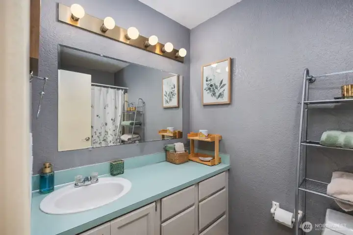 Bathroom with single-sink vanity, large wall mirror, overhead vanity lighting, and tub-shower combination