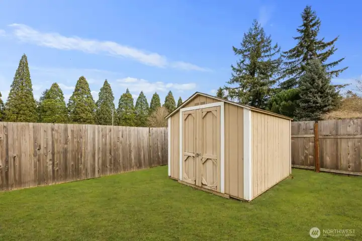 Fully fenced backyard featuring a detached storage shed and expansive grassy area, offering practical space for tools, hobbies, or seasonal storage