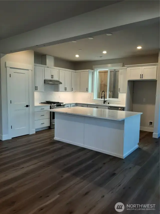 Open kitchen with quartz counters and generous island features gas range, dishwasher and microwave