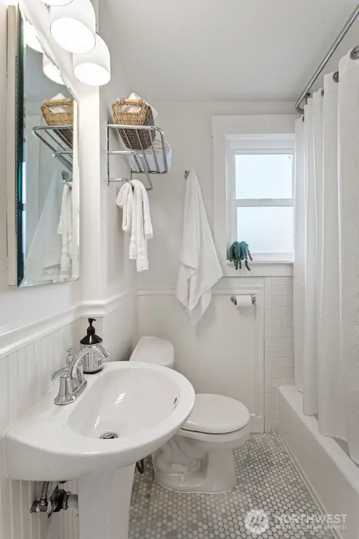 Main floor full bath features marble hex tile flooring with in-floor heat, a newly refinished bathtub and subway tile surround and new pedestal sink.