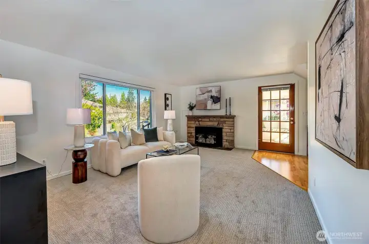 One of two living areas, the main-floor living room featuring a beautiful MCM stone surround wood-burning fireplace and large windows. This versatile floor plan offers two separate areas for everyone to spread out and enjoy. New carpet and paint throughout!