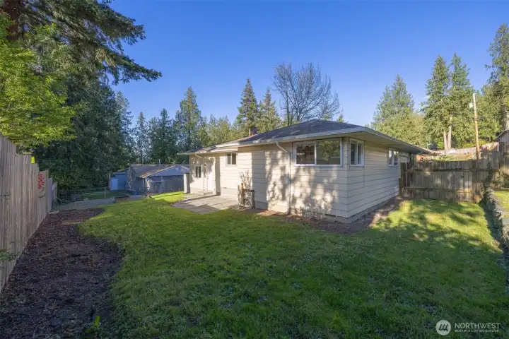 Looking at the far corner of the fully fenced rear yard with the back patio and the fire pit area beyond.