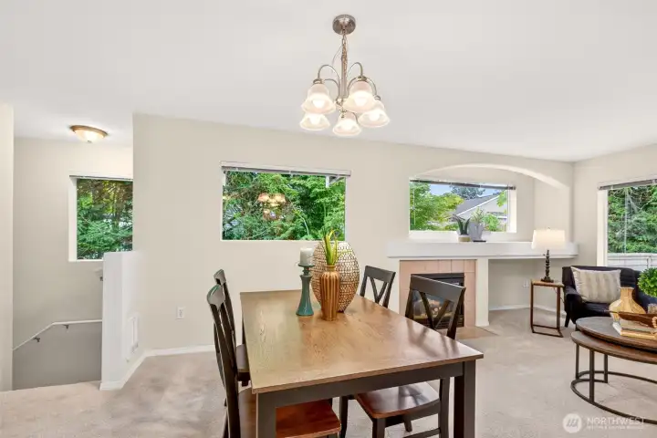 A cozy tile-surround gas fireplace anchors the living space, offering a warm focal point on cool Pacific Northwest evenings. Multiple windows keep the room airy and bright while leafy views provide a sense of privacy.
