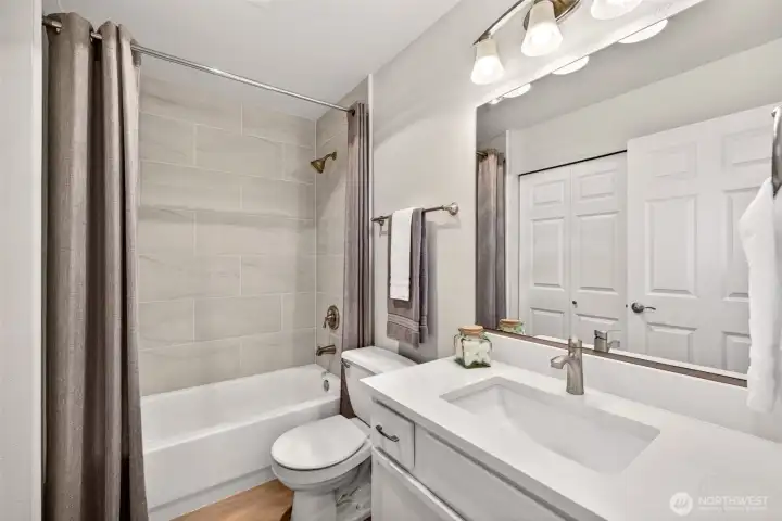 A beautifully updated bath features new tile surround, a quartz counter with undermount sink, and new fixtures for a clean, spa-like feel. The tub-shower combination and generous mirror make it both practical and polished.