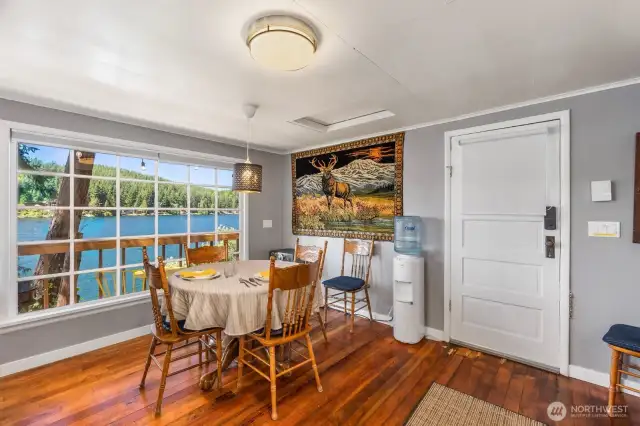 Dining area with lodge-style decor, original rustic wood floors, and front door access. Large window overlooks the deck and lake.