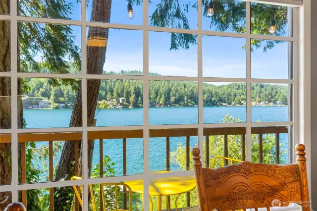 Lake view from inside the cabin through large grid window framed by trees and deck railing.