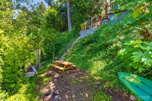 Lower lakefront area with firepit, picnic table, shed and bin storage, and kayak.
