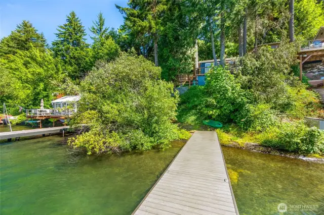 Dock view towards bank and cabin yard, with lush trees.