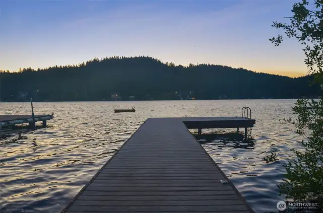 Dock at sunset with calm water and hills silhouetted across the lake.