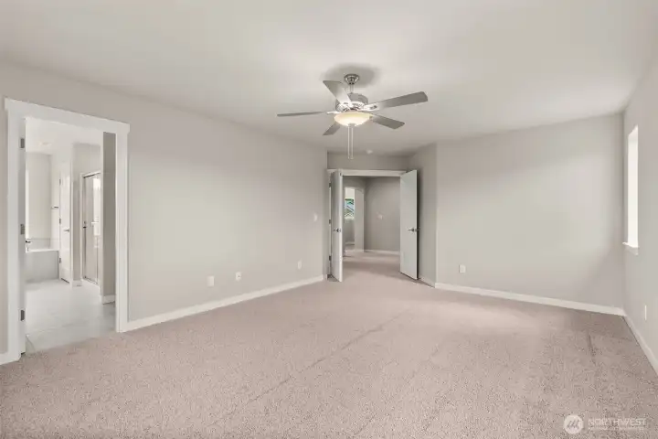 Spacious primary bedroom features vaulted ceilings, large windows for natural light, and a ceiling fan for added comfort.