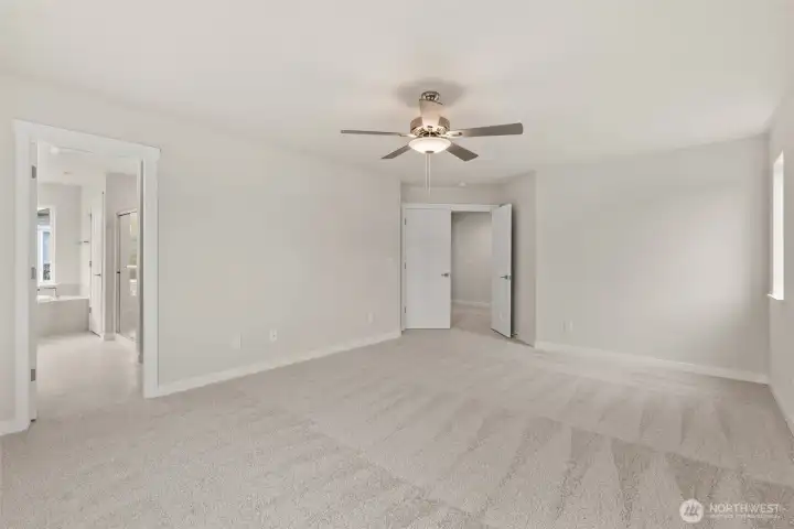 Spacious primary bedroom features vaulted ceilings, large windows for natural light, and a ceiling fan for added comfort.