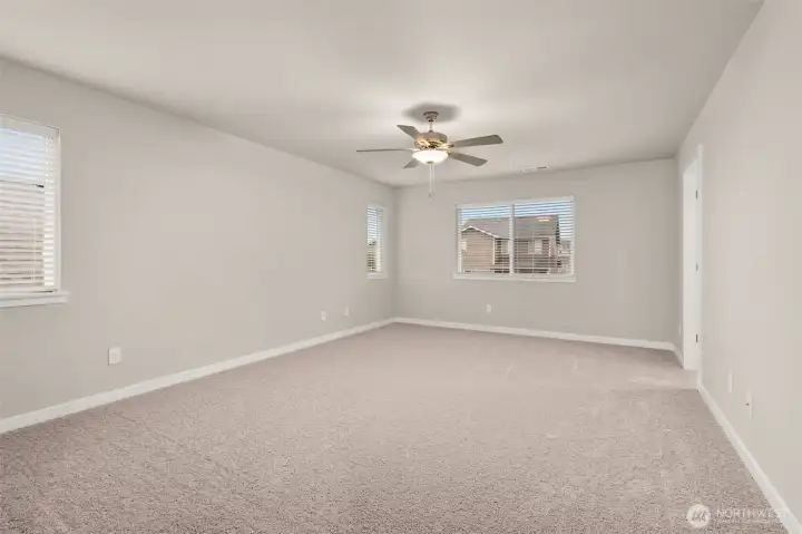 Spacious primary bedroom features vaulted ceilings, large windows for natural light, and a ceiling fan for added comfort.