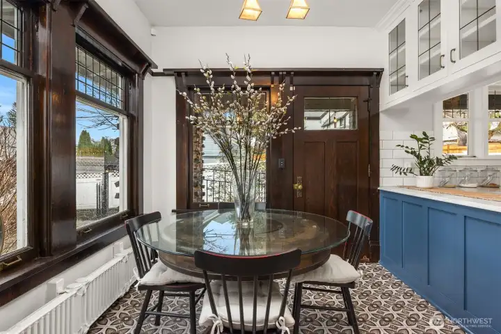 A charming breakfast nook blends historic character with modern function. Original wood-trimmed windows, patterned tile floors, and a cozy built-in feel create an inviting space for morning coffee or casual meals, seamlessly connected to the kitchen while overlooking the garden beyond.