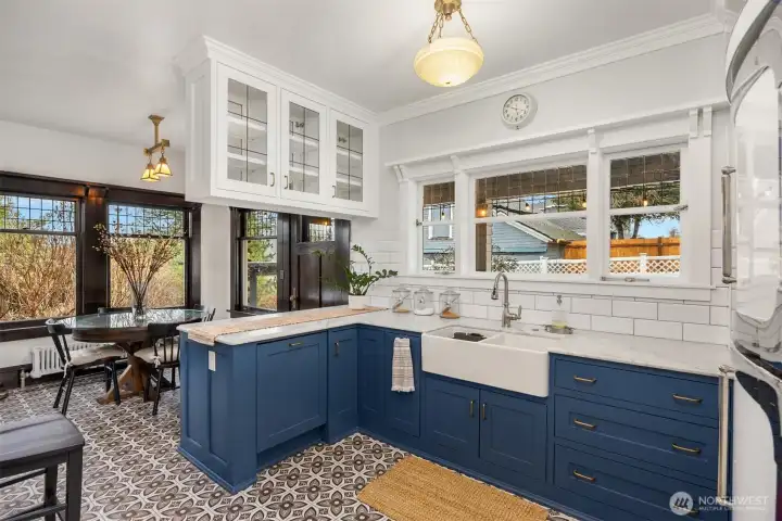 A thoughtfully renovated kitchen blends historic charm with modern design. Custom cabinetry in a rich blue tone, marble-style counters, and period-inspired lighting connect seamlessly to the breakfast nook, creating a warm, functional heart of the home.