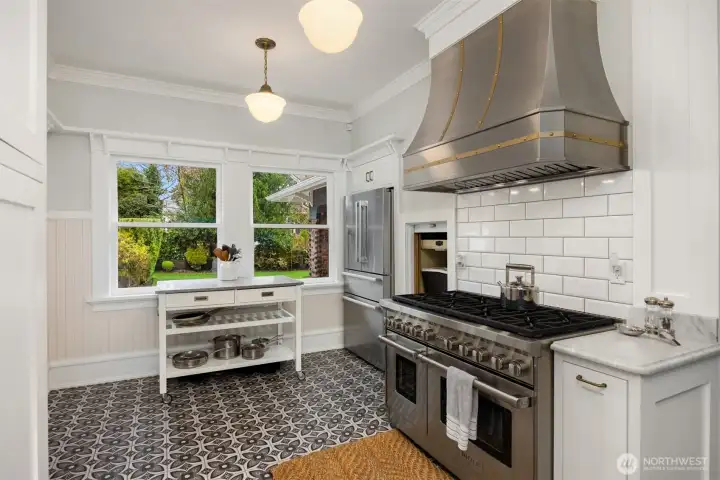 Designed for both beauty and performance, the kitchen showcases a professional-grade 8-burner double range/oven beneath a custom hood, surrounded by crisp cabinetry and historic trim—an inspired setting for serious cooks and casual meals alike.