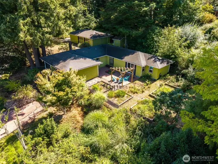 An aerial view of the property shows one lot in the upper left corner with the shop, where easy access to the side entrance of the home awaits.  In the foreground see a charming courtyard, and lush gardens with water view.
