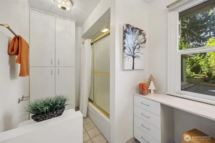 Around the corner from the kitchen and living spaces, a full bath room marks the entry to the long sleeping wing.  The combination tub and shower with glass doors sit adjacent to a large laundry cupboard.