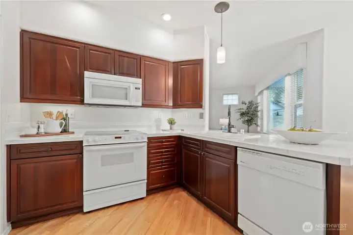 It features abundant cabinetry, porcelain tile countertops, white-on-white appliances, undercabinet lighting, and gleaming hardwood floors.