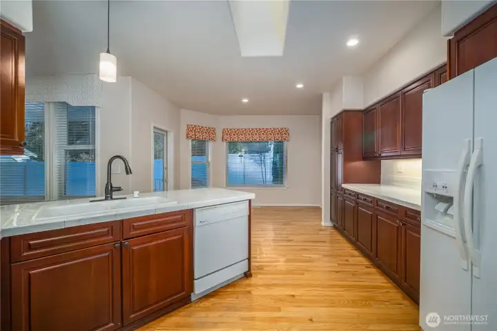 It features abundant cabinetry, porcelain tile countertops, white-on-white appliances, undercabinet lighting, and gleaming hardwood floors.