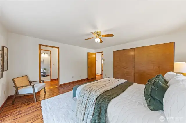 Spacious primary suite with warm wood-style floors, double closets, and private en suite bath
