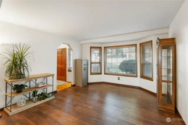 Second view of living room off front of home with newer wood flooring built in blinds and lots of windows facing to front of home