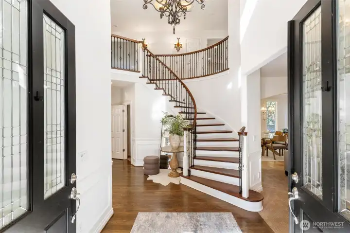Elegant entryway showcasing a dramatic curved staircase with dark wood treads and a classic chandelier.