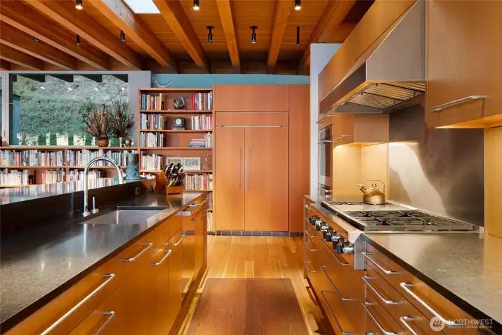 The chef’s kitchen features custom cabinetry, expansive stone counters, professional appliances, and skylit wood beam ceilings, blending warm natural materials with refined modern design.